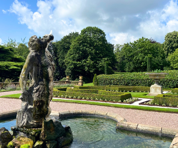 A stone statue in the middle of a fountain next to a landscaped garden.